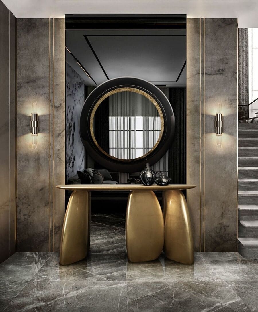 A modern entryway with a luxurious gold sideboard, a black and gold mirror and modern wall lamps.